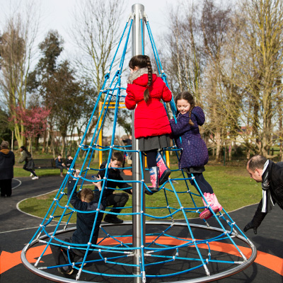 A rope cone climber which also spins at a playground, children are playing on it.